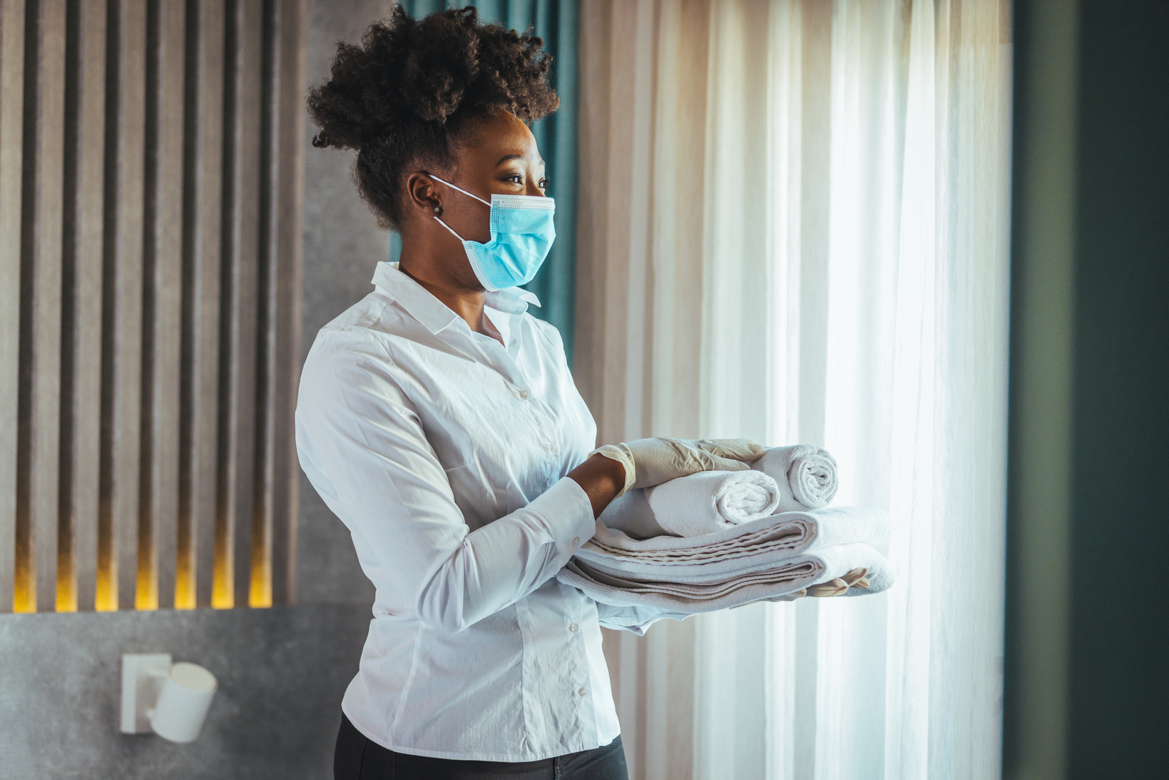 Maid with face protective mask cleaning a hotel room during pandemic.